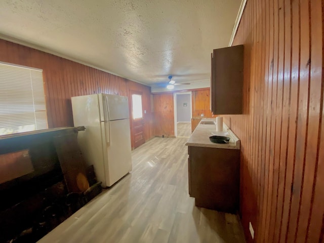 kitchen featuring wood walls, a textured ceiling, light wood-type flooring, white refrigerator, and ceiling fan