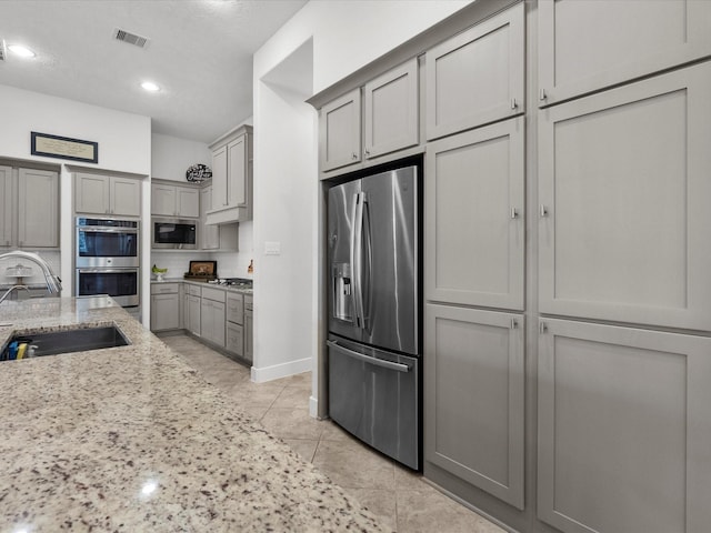 kitchen featuring light tile patterned flooring, sink, gray cabinetry, stainless steel appliances, and light stone countertops