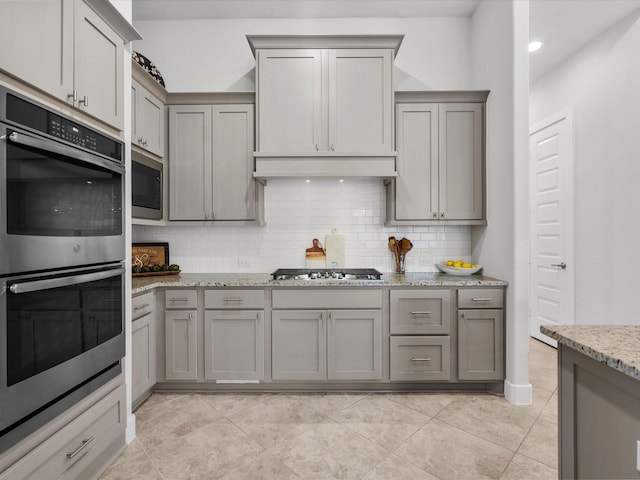 kitchen featuring light stone counters, backsplash, gray cabinets, and stainless steel appliances