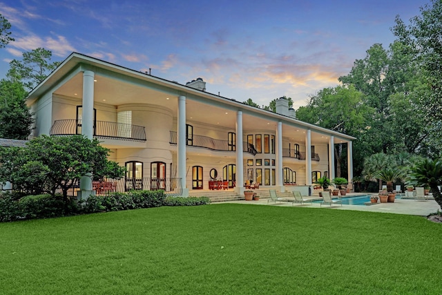 back house at dusk featuring a lawn and a balcony