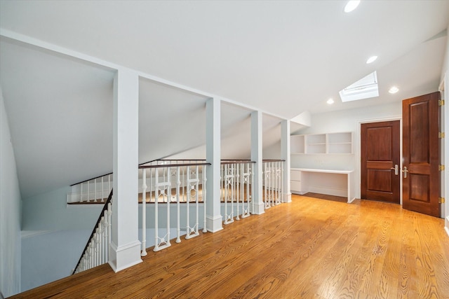 hallway with lofted ceiling with skylight and light wood-type flooring