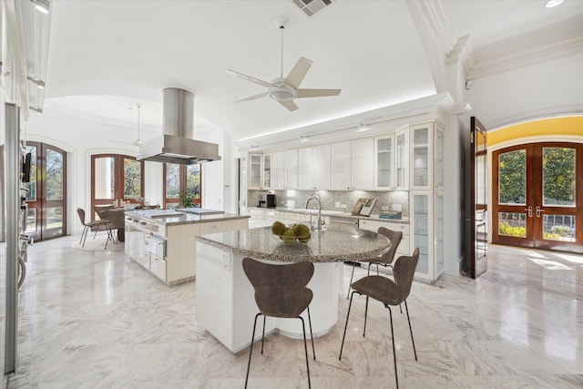 kitchen with stone counters, island range hood, white cabinets, a kitchen island with sink, and french doors