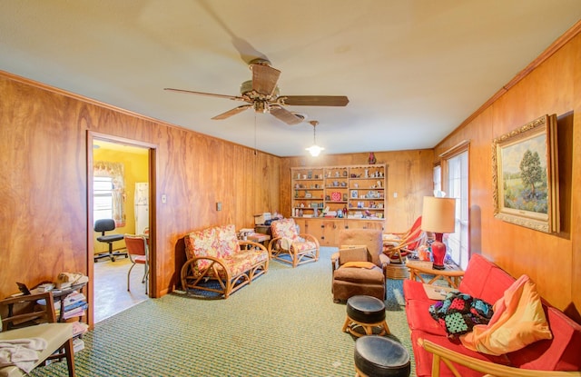 living area featuring ceiling fan, ornamental molding, wooden walls, and carpet floors