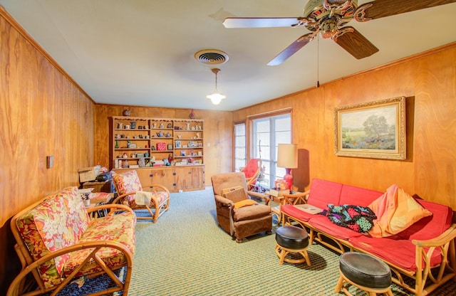 living area with wood walls, crown molding, carpet floors, built in features, and ceiling fan