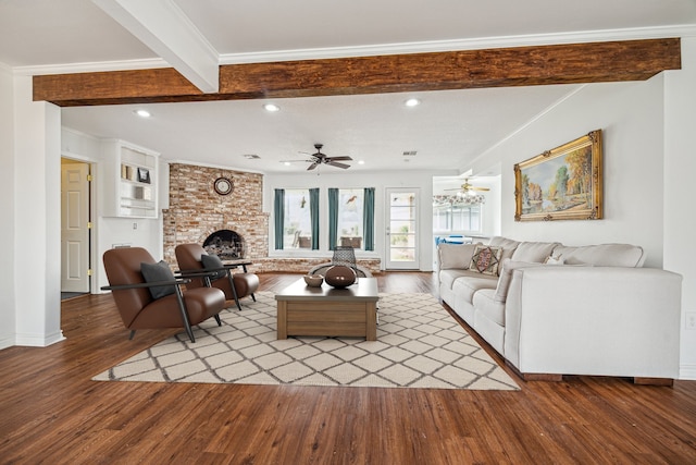 living room with beamed ceiling, wood-type flooring, ceiling fan, crown molding, and a brick fireplace