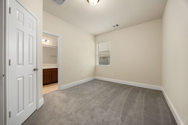 unfurnished bedroom featuring light carpet and ensuite bath