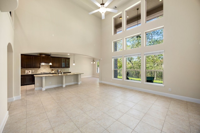 unfurnished living room with sink, a towering ceiling, ceiling fan, and light tile patterned flooring