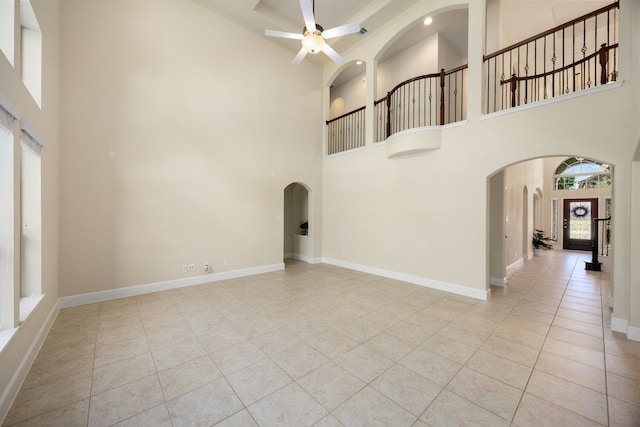 unfurnished living room with light tile patterned floors, a towering ceiling, and ceiling fan