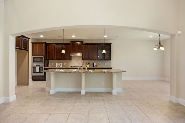 kitchen featuring light stone counters, an inviting chandelier, decorative light fixtures, appliances with stainless steel finishes, and an island with sink