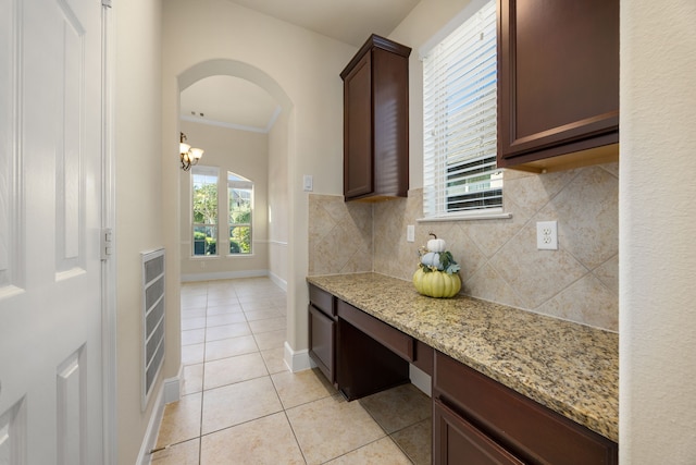 kitchen featuring light tile patterned floors, backsplash, light stone counters, dark brown cabinetry, and ornamental molding