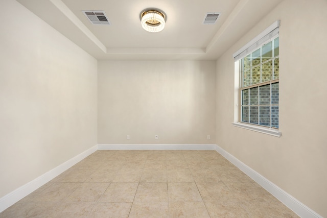 tiled empty room featuring a tray ceiling