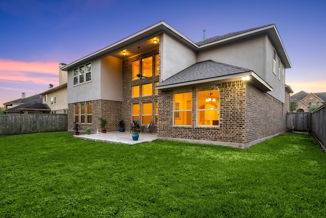 back house at dusk with a patio and a lawn