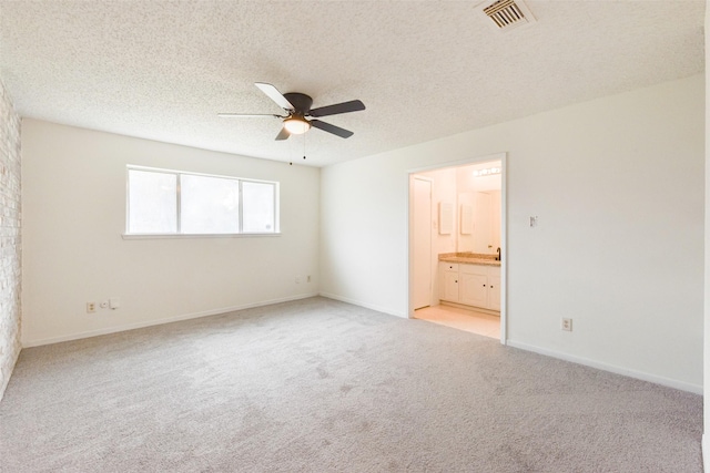 unfurnished bedroom with ceiling fan, light colored carpet, a textured ceiling, and ensuite bathroom