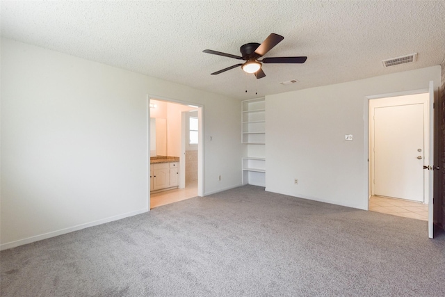 unfurnished bedroom featuring ceiling fan, ensuite bath, light carpet, and a textured ceiling