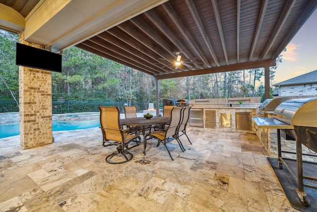 patio terrace at dusk with ceiling fan, area for grilling, and a swimming pool with hot tub