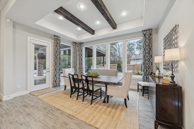 dining area with a tray ceiling, beam ceiling, and light wood-type flooring