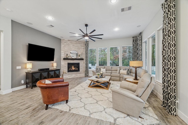 living room featuring ceiling fan, a stone fireplace, and light hardwood / wood-style floors