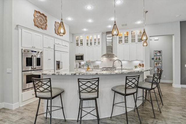 kitchen with a large island, white cabinetry, built in appliances, and wall chimney range hood