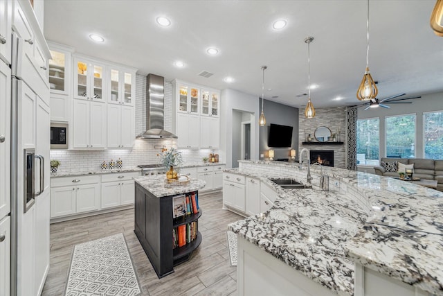 kitchen featuring white cabinetry, wall chimney exhaust hood, sink, and an island with sink