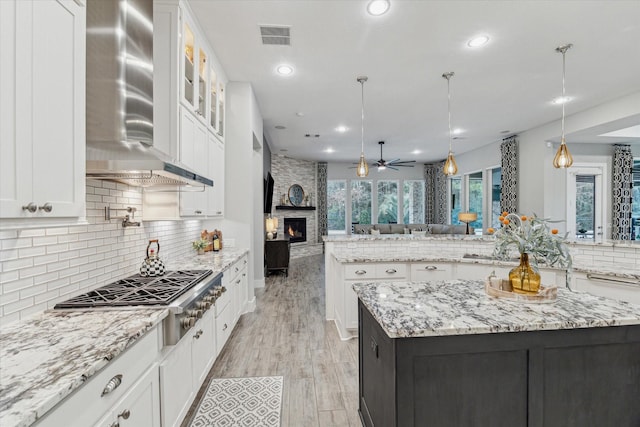 kitchen with hanging light fixtures, wall chimney exhaust hood, a center island, white cabinets, and stainless steel gas stovetop