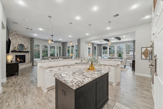 kitchen with a large island, hanging light fixtures, light stone countertops, and white cabinets