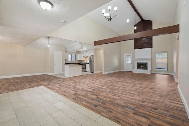 unfurnished living room with a chandelier, a textured ceiling, a large fireplace, beamed ceiling, and light hardwood / wood-style floors