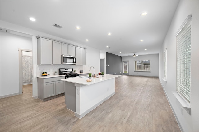 kitchen featuring sink, light hardwood / wood-style flooring, gray cabinets, stainless steel appliances, and a center island with sink