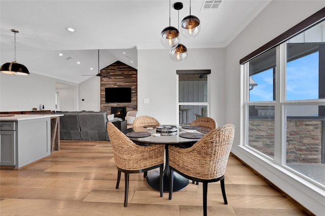 dining room featuring crown molding, vaulted ceiling, light wood-type flooring, ceiling fan, and a fireplace