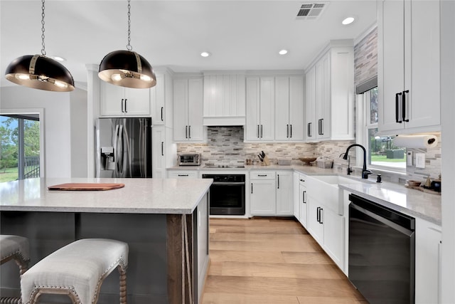 kitchen featuring pendant lighting, sink, white cabinetry, black appliances, and light wood-type flooring