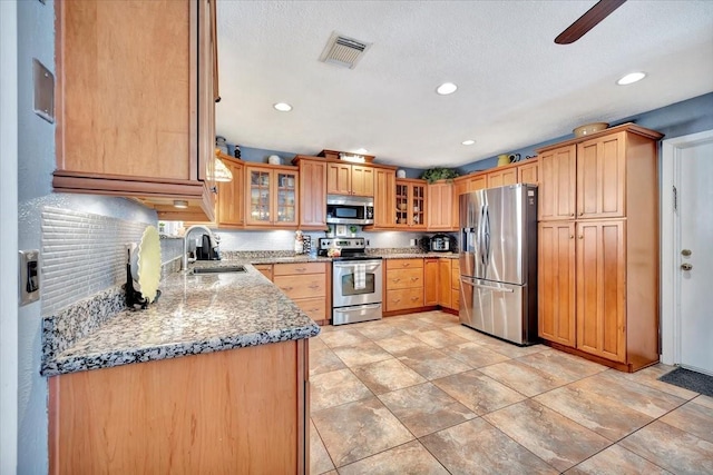 kitchen with sink, ceiling fan, backsplash, stainless steel appliances, and light stone counters