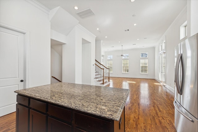 kitchen with hardwood / wood-style floors, stainless steel refrigerator, a center island, crown molding, and light stone countertops