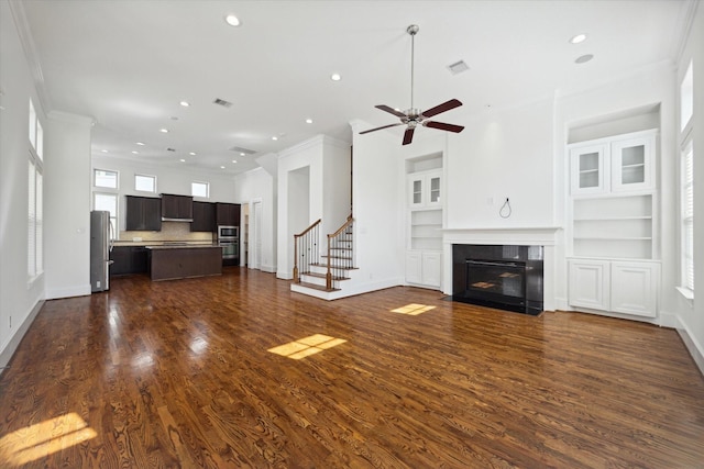 unfurnished living room featuring crown molding, dark hardwood / wood-style floors, ceiling fan, and built in shelves