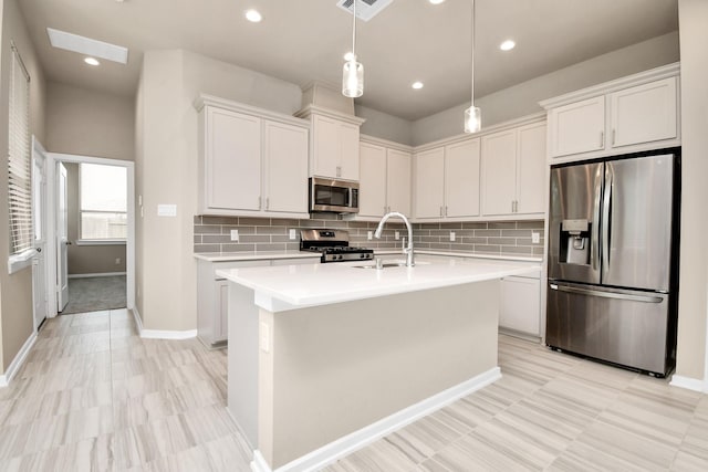 kitchen featuring sink, white cabinetry, decorative light fixtures, appliances with stainless steel finishes, and a kitchen island with sink