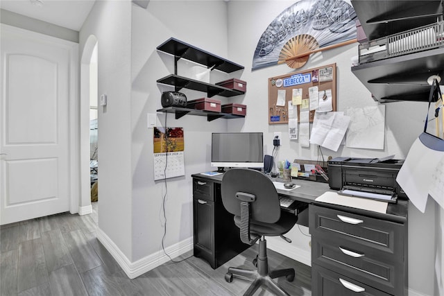 office with baseboards, arched walkways, and wood finish floors