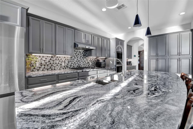 kitchen with pendant lighting, dark stone countertops, backsplash, gray cabinetry, and stainless steel appliances