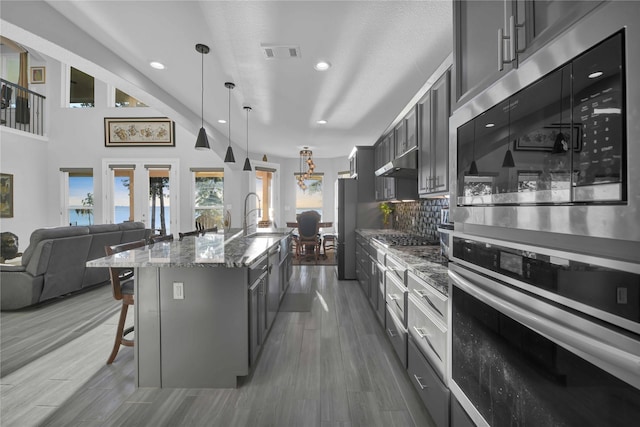 kitchen featuring visible vents, light stone countertops, under cabinet range hood, a kitchen breakfast bar, and stainless steel appliances