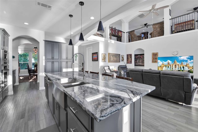 kitchen featuring gray cabinetry, pendant lighting, ceiling fan, light stone countertops, and a kitchen island with sink