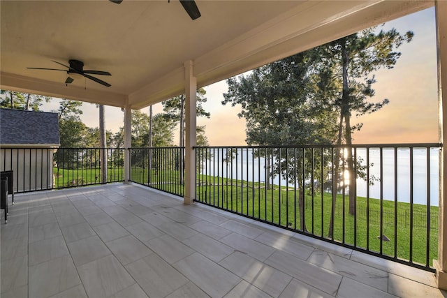 patio terrace at dusk with a water view, ceiling fan, and a lawn