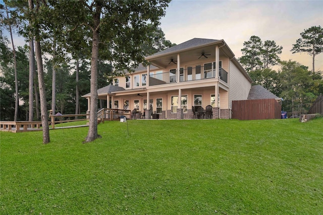 back of house with a yard, a balcony, a ceiling fan, and fence