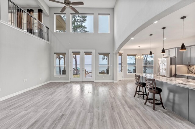 living room featuring ceiling fan with notable chandelier, french doors, and light wood-type flooring