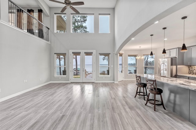 living room featuring french doors, baseboards, light wood-style floors, and ceiling fan with notable chandelier