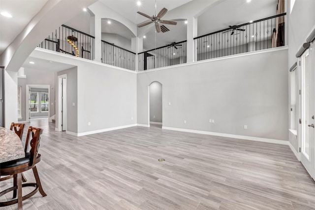 living area featuring ceiling fan, baseboards, arched walkways, and light wood-style flooring