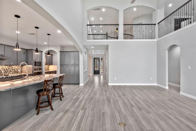 kitchen with light wood finished floors, gray cabinetry, oven, light stone countertops, and a breakfast bar