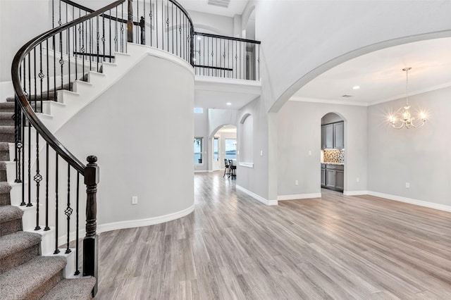 foyer with ornamental molding, a towering ceiling, a chandelier, and light hardwood / wood-style floors