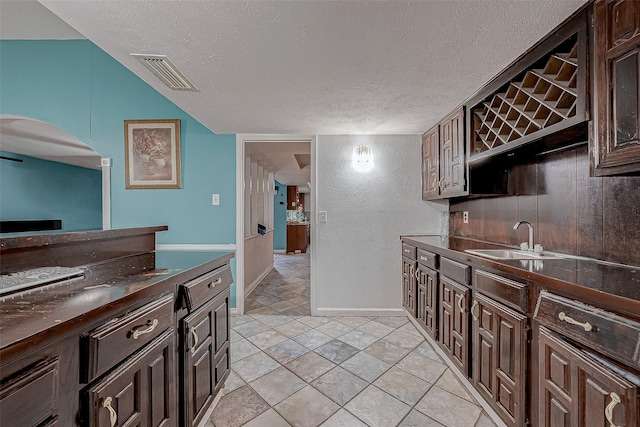 kitchen with dark brown cabinetry, sink, a textured ceiling, and light tile patterned floors