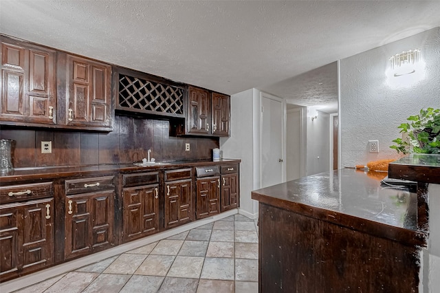 kitchen with dark brown cabinetry, sink, a textured ceiling, and light tile patterned flooring