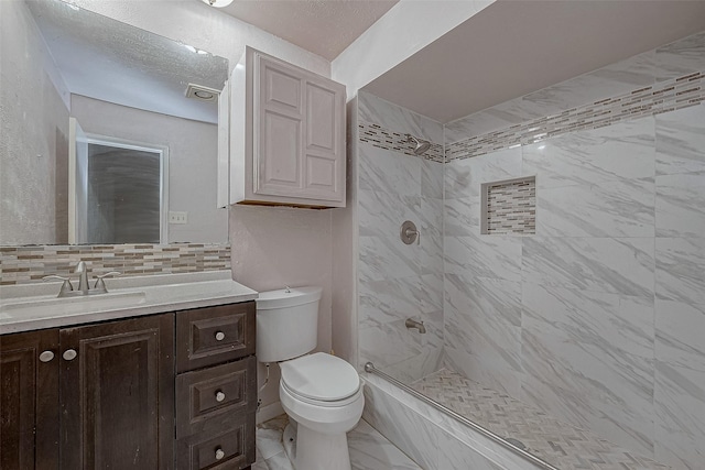 bathroom featuring tasteful backsplash, vanity, a tile shower, and toilet