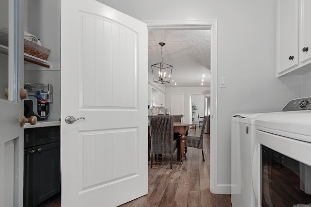 clothes washing area featuring dark hardwood / wood-style floors, cabinets, washing machine and clothes dryer, a textured ceiling, and an inviting chandelier