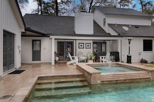 back of property with a swimming pool with hot tub, a patio, french doors, and pool water feature