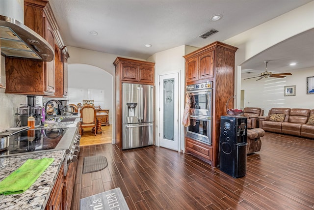 kitchen featuring appliances with stainless steel finishes, dark wood-type flooring, wall chimney range hood, and light stone counters